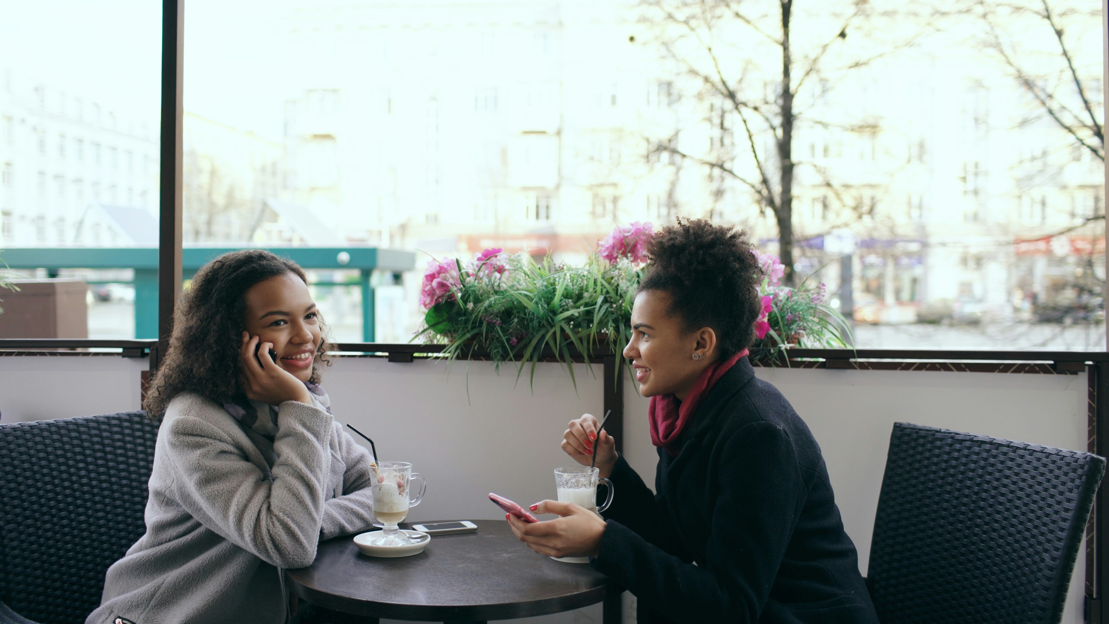 Friends laughing over coffee at a sidewalk café, a European street softly out of focus behind them