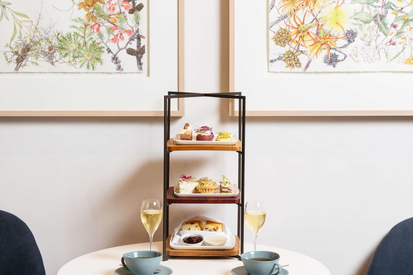 Afternoon tea served at a table at COMO The Treasury, beneath botanical artworks