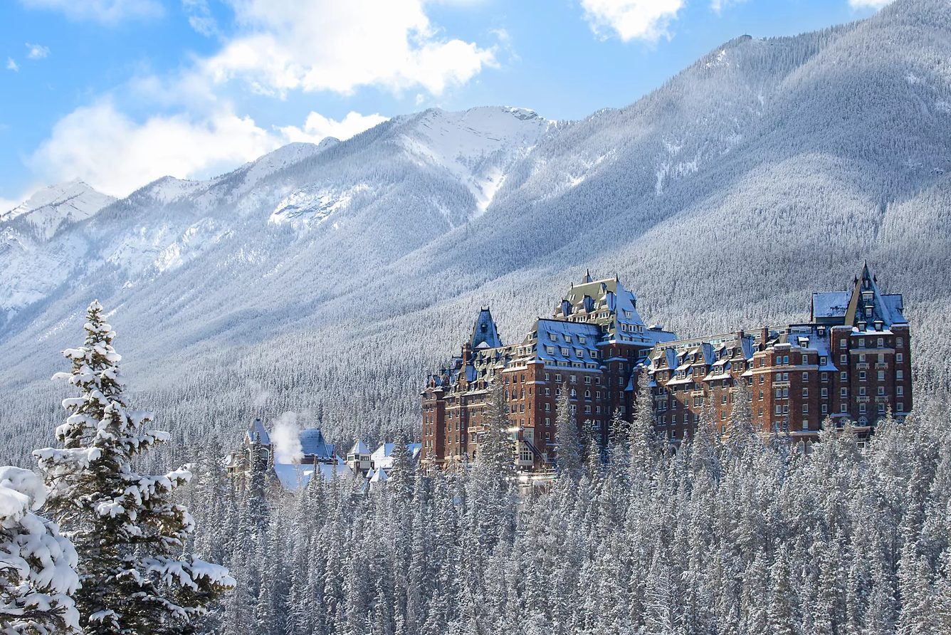 Fairmont Banff Springs in winter, surrounded by snow-covered forest below the Canadian Rockies