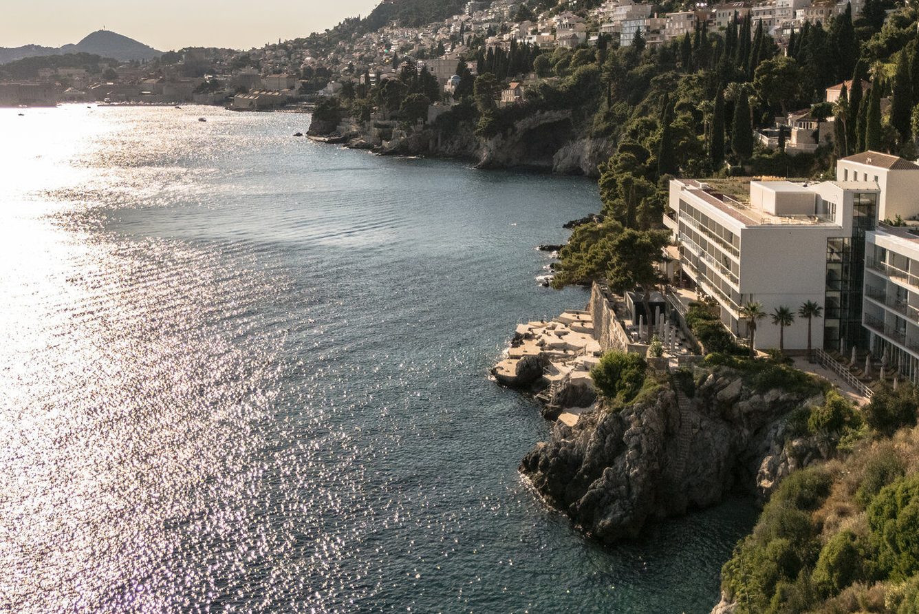 Aerial view of Villa Dubrovnik's white buildings on the cliffs above the Adriatic, with Dubrovnik Old Town in the distance
