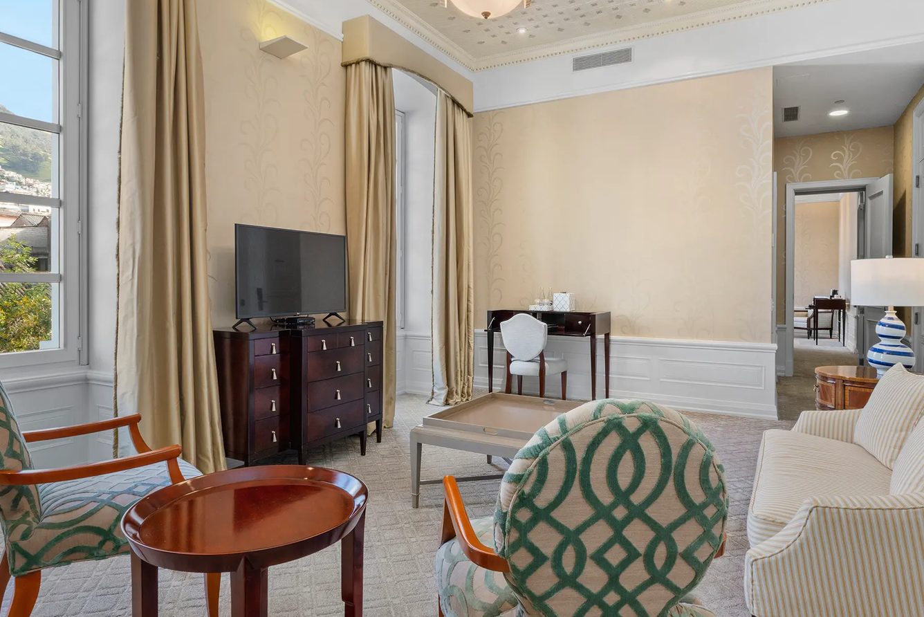 Suite living room at Casa Gangotena with green-patterned armchairs, a striped sofa and tall draped windows, Quito