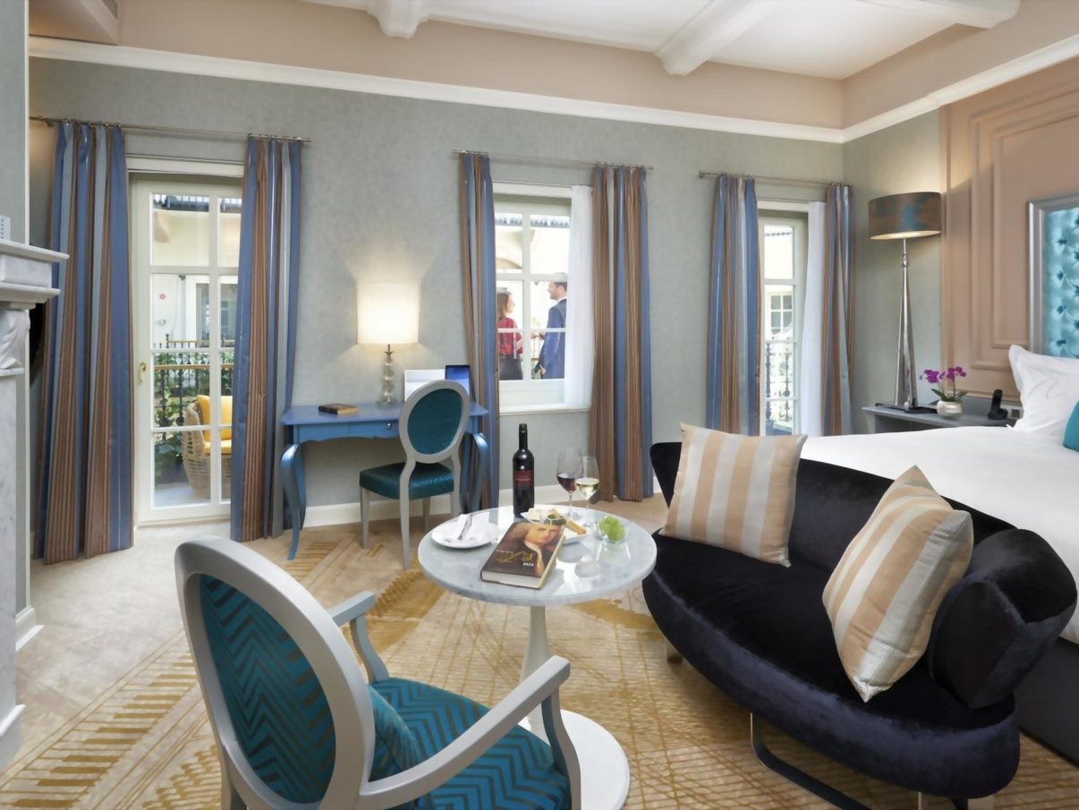 A guest room at Aria Hotel Budapest, with a marble fireplace, chaise longue and tall windows