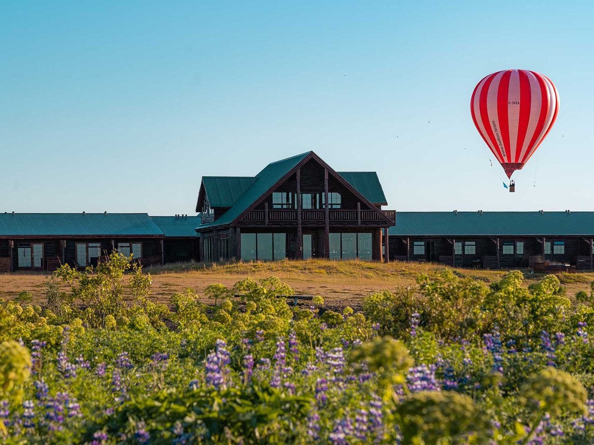 Hotel Rangá's log-built lodge in daylight, with lupine in the foreground and a hot-air balloon overhead