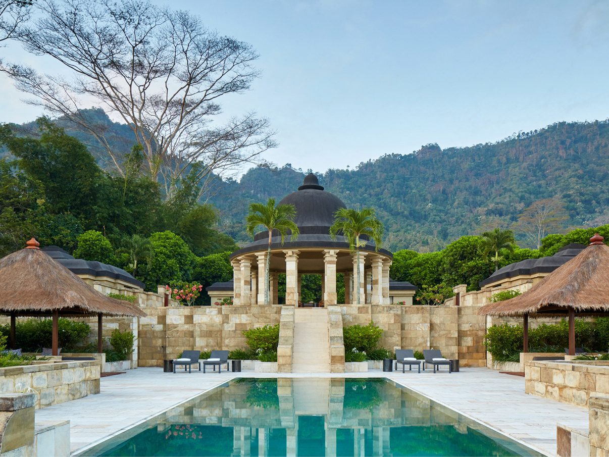 Amanjiwo's main swimming pool and stone pavilion below forested hills near Borobudur