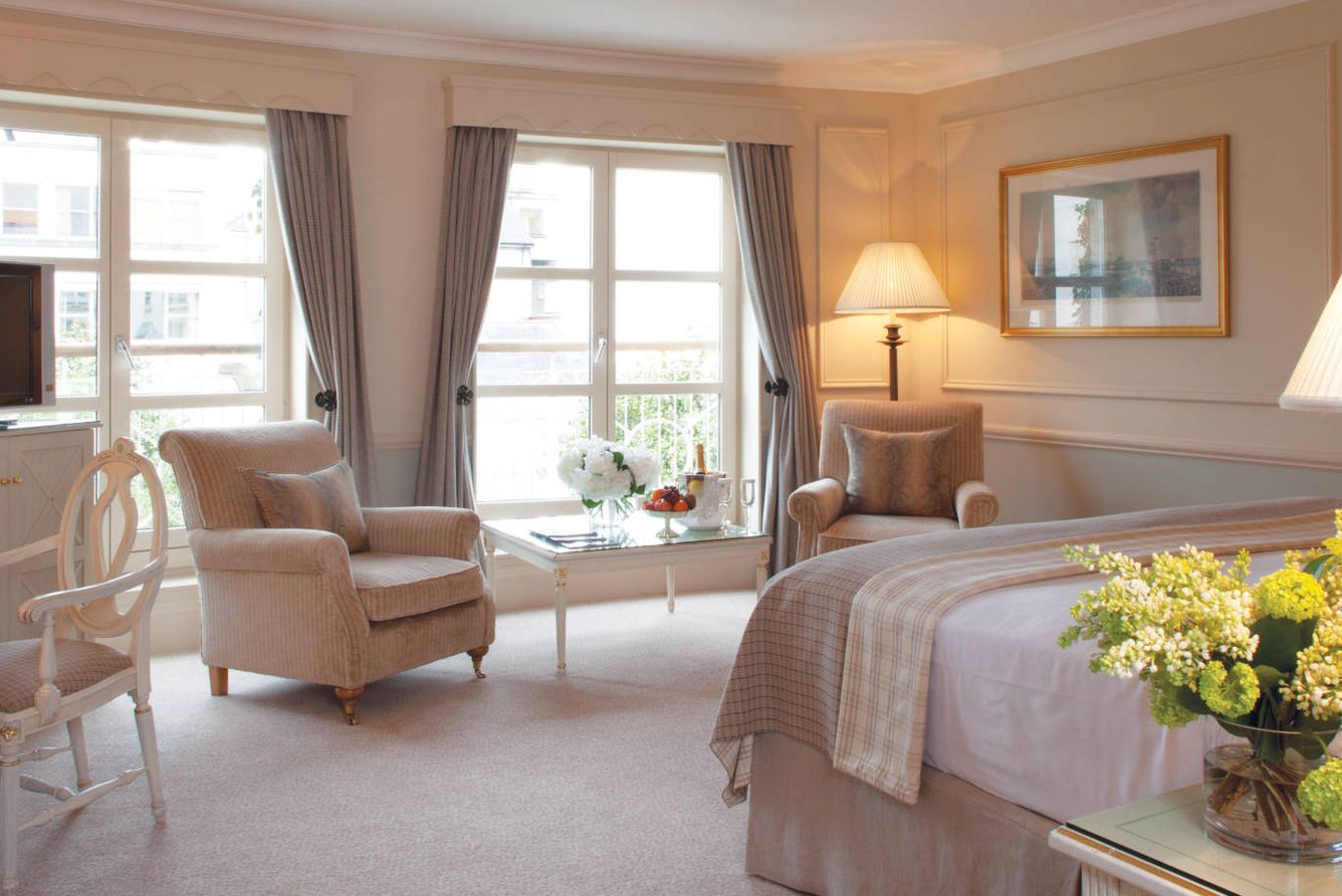 A bedroom at The Merrion Hotel with armchairs and garden-view windows