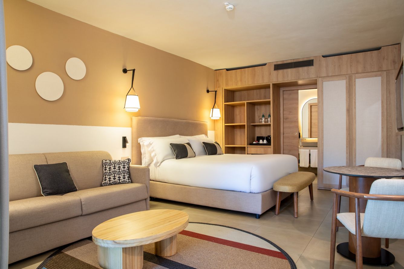 A renovated room at Mangia's Sardinia Resort — king bed, sofa and wood shelving