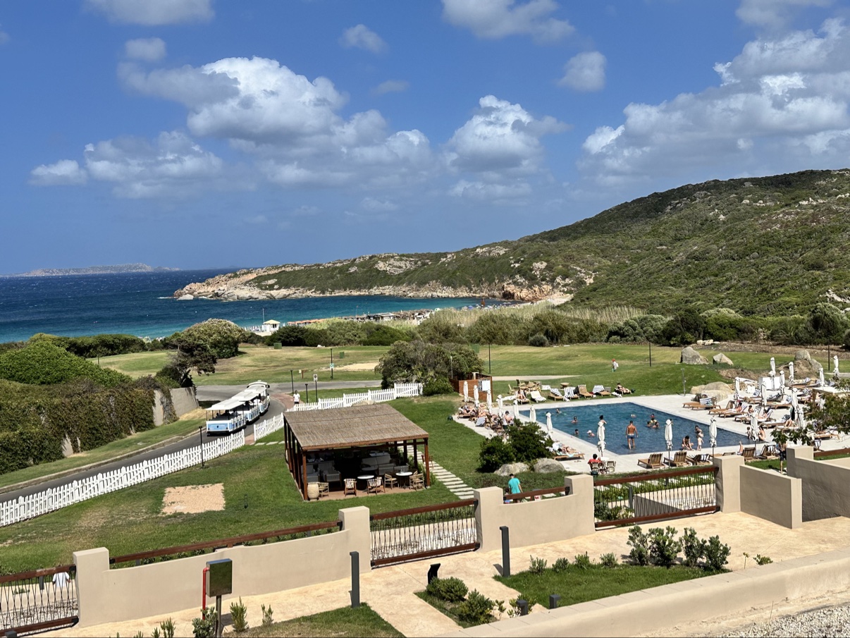 The main pool and grounds at Mangia's Sardinia Resort, looking out to the beach and headland at La Marmorata