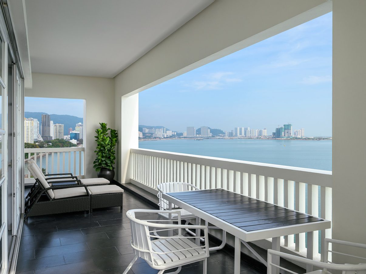 A corner-suite balcony at the Eastern & Oriental Hotel, with loungers and a table overlooking the Penang Strait