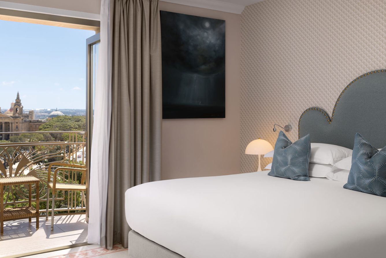 A Valletta Suite bedroom at The Phoenicia Malta opening onto a balcony over the city