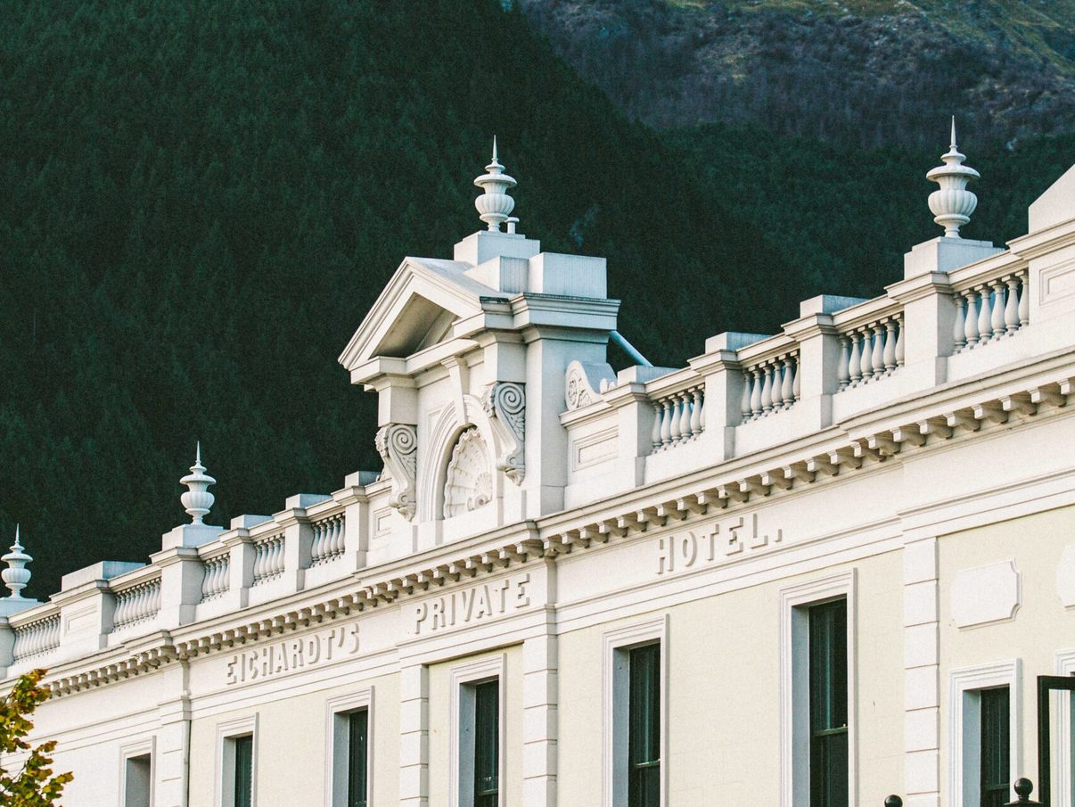 The white heritage facade of Eichardt's Private Hotel on Marine Parade in Queenstown, with the mountains behind