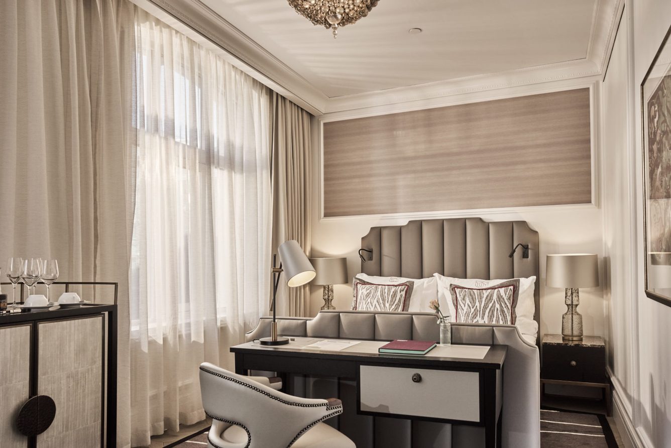 A bedroom at Britannia Hotel with a desk, armchair and sheer-curtained windows