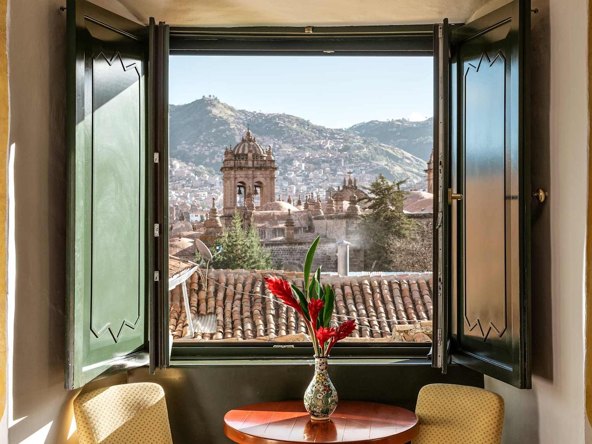A Monasterio guest-room window framing Cusco's tiled rooftops and a church tower beyond