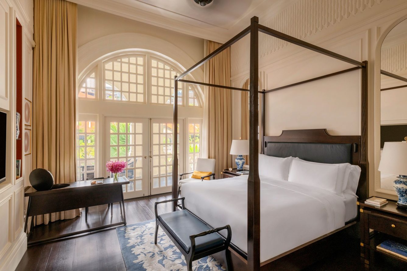 A Raffles suite bedroom with a four-poster canopy bed and arched French windows.