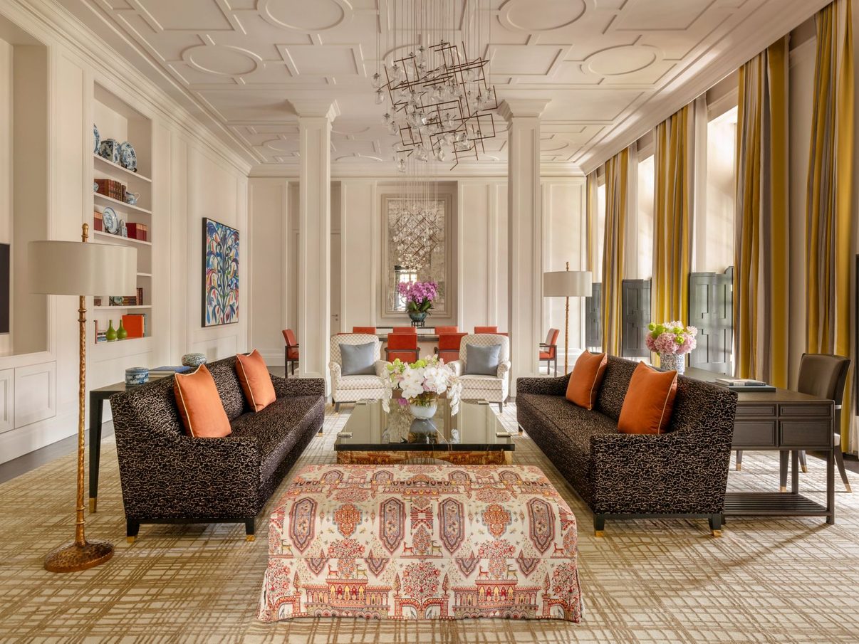 The grand parlour of a Raffles suite, with sofas arranged around a patterned rug beneath an ornate ceiling.