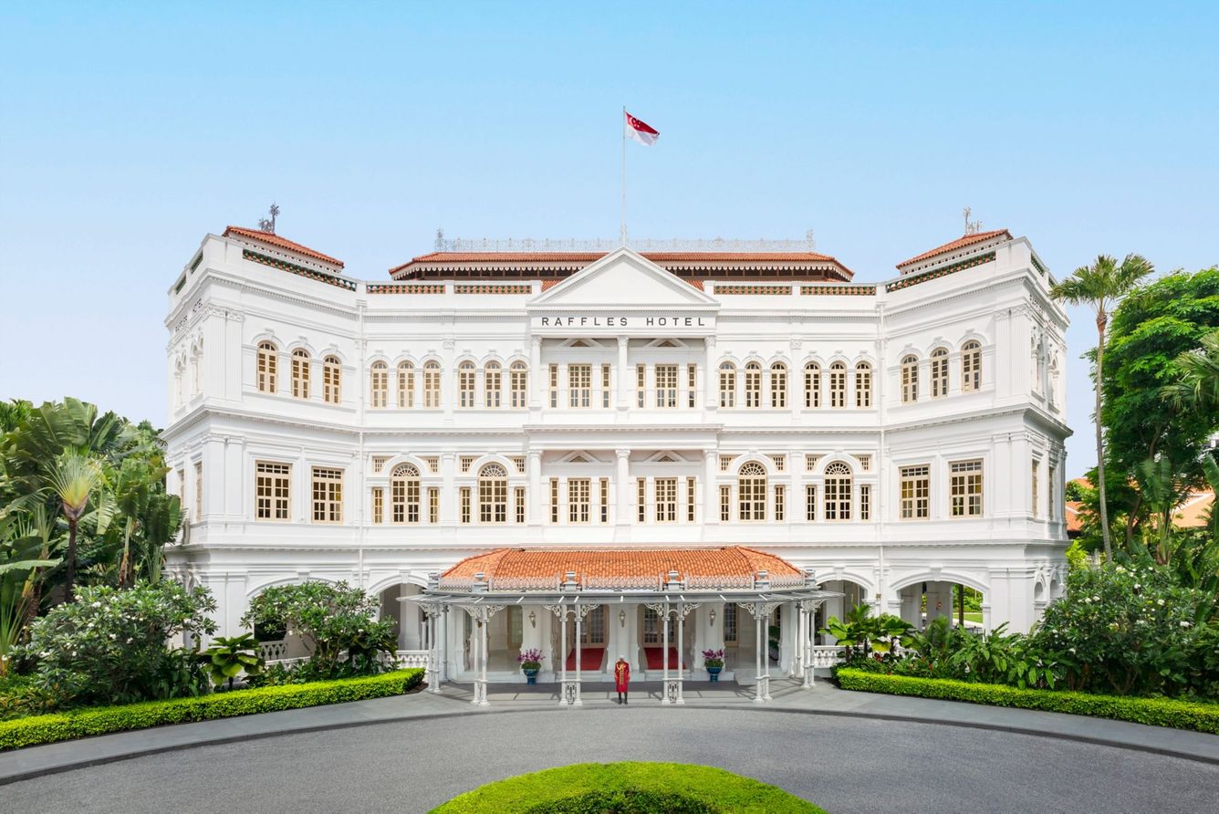 The white colonial facade of Raffles Hotel Singapore, seen across its circular drive on Beach Road.
