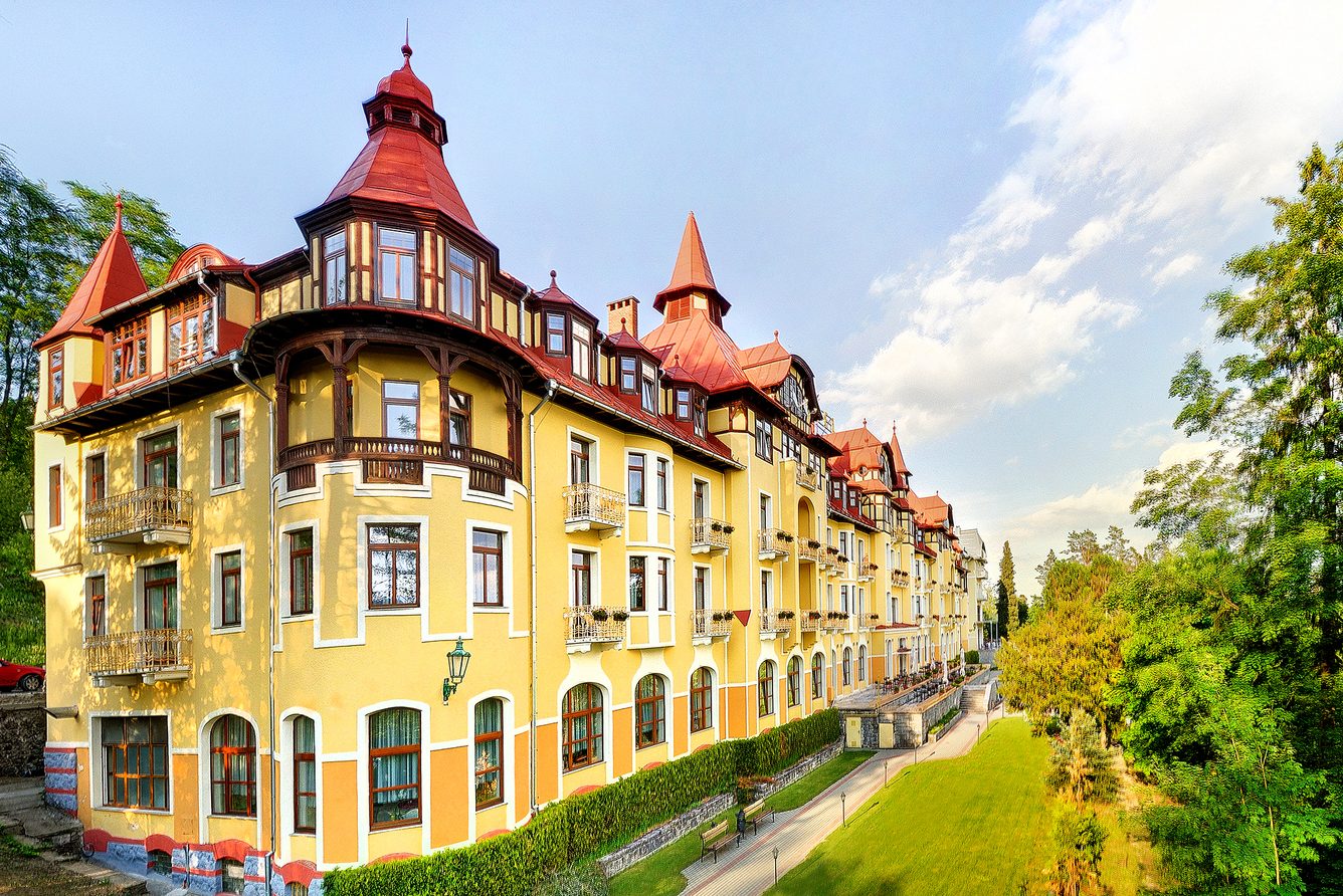 The Art Nouveau facade and red turret of Grandhotel Praha seen from its park