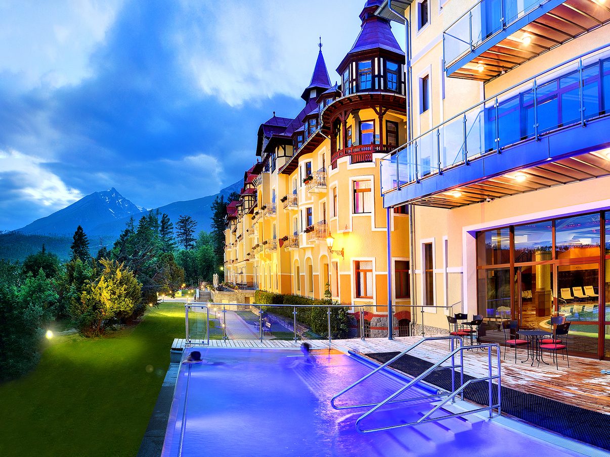 Grandhotel Praha lit up at dusk, its outdoor pool in the foreground and the Tatra peaks behind