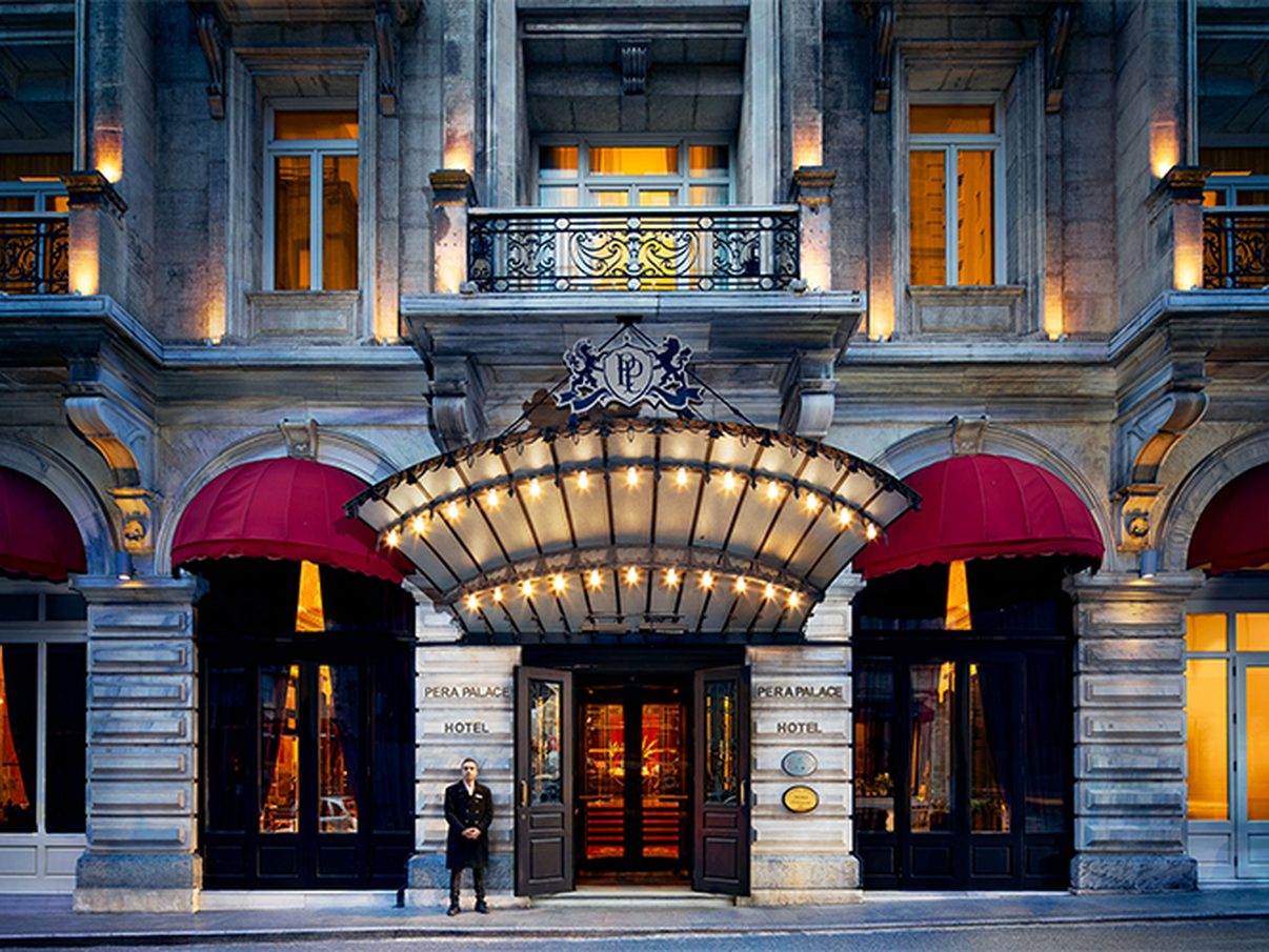 The illuminated entrance canopy and stone facade of Pera Palace Hotel at dusk
