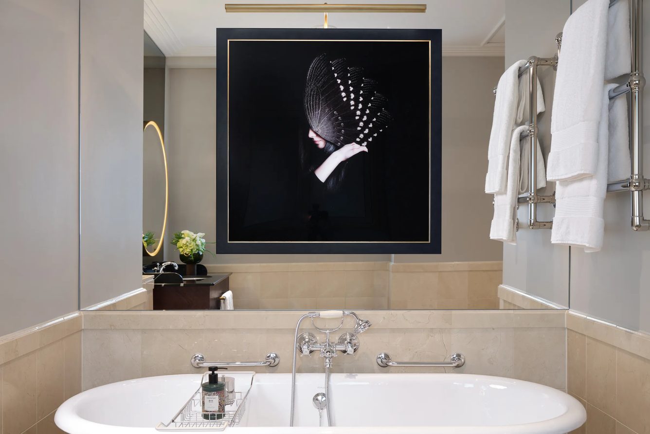 A marble bathroom at The Savoy with a freestanding bath, heated towel rails and a framed feather artwork